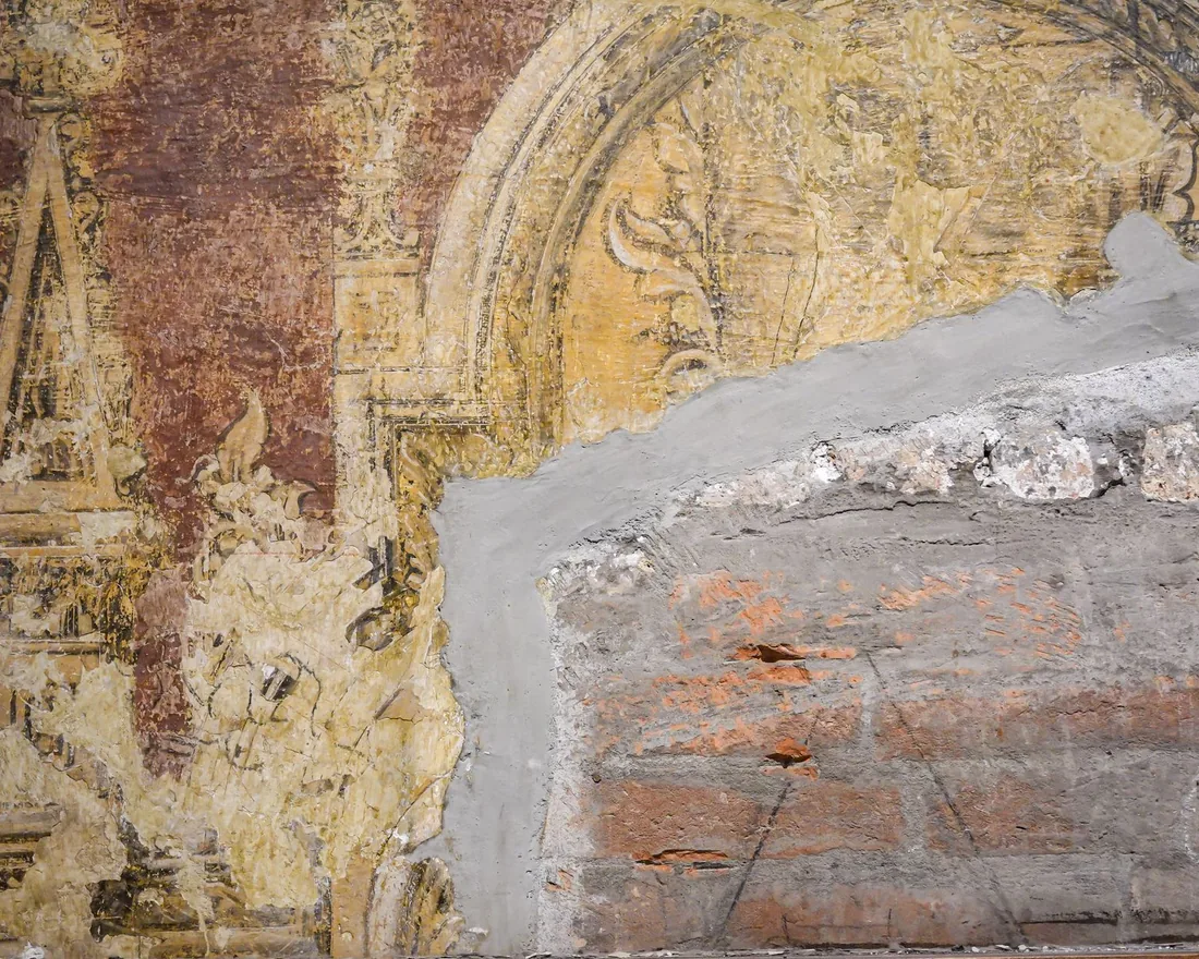 Muro con una pintura mural antigua parcialmente conservada, con zonas de mortero perdido y restos de color